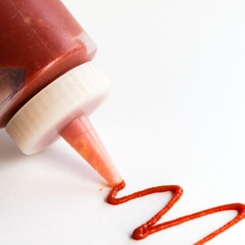 A squiggle of spicy ketchup next to a bottle of ketchup.